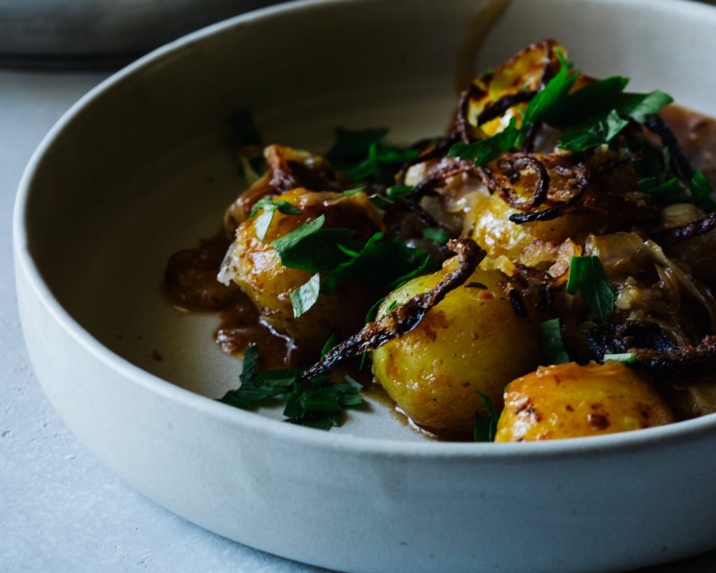 Nahaufnahme eines cremigen Kartoffelgerichts mit frischer Petersilie und knusprig gebratenen Zwiebeln in einer hellen Keramikschale. Dieses herzhafte Gericht gehört zu den beliebten veganen Rezepten und zeigt, wie köstlich und vielseitig pflanzliche Küche sein kann.
