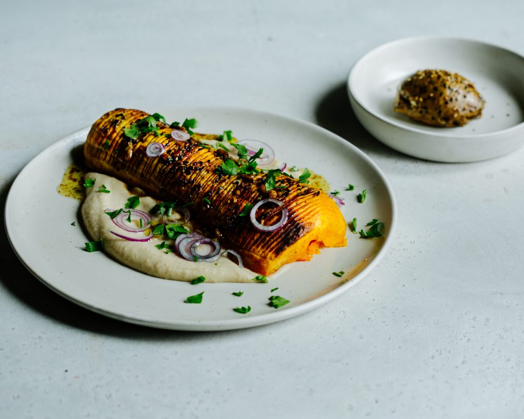 Butternut Kürbis Rezept: knusprig gebackener Kürbis auf cremiger Bohnencreme, serviert mit roten Zwiebeln und frischen Kräutern – perfektes veganes Herbstgericht.