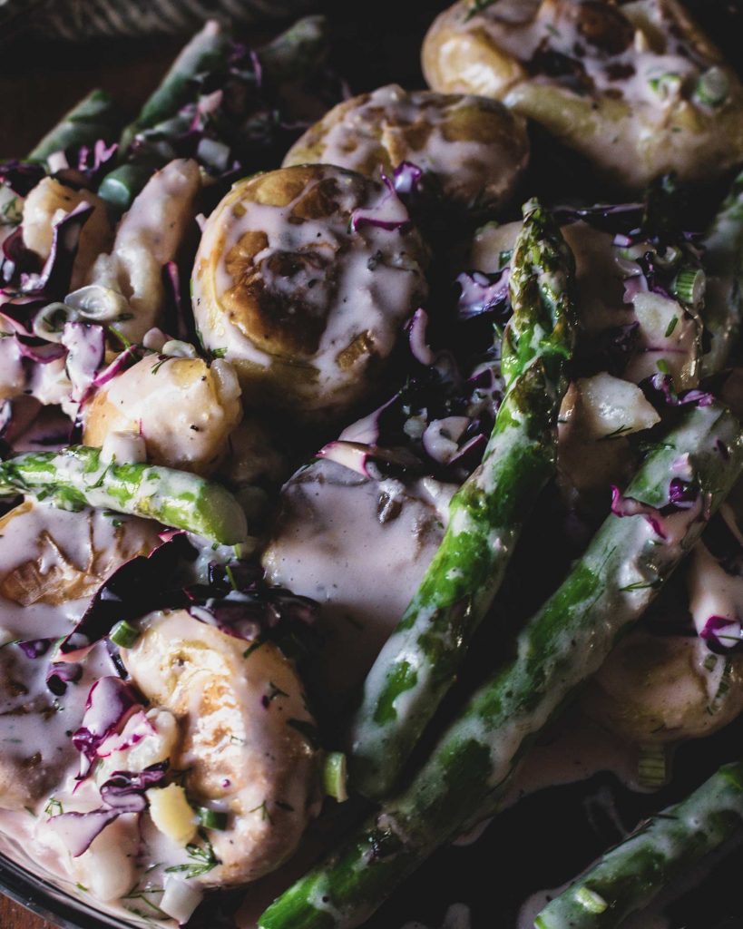 Veganer Kartoffelsalat mit Ofenkartoffeln und grünem Spargel auf Teller serviert