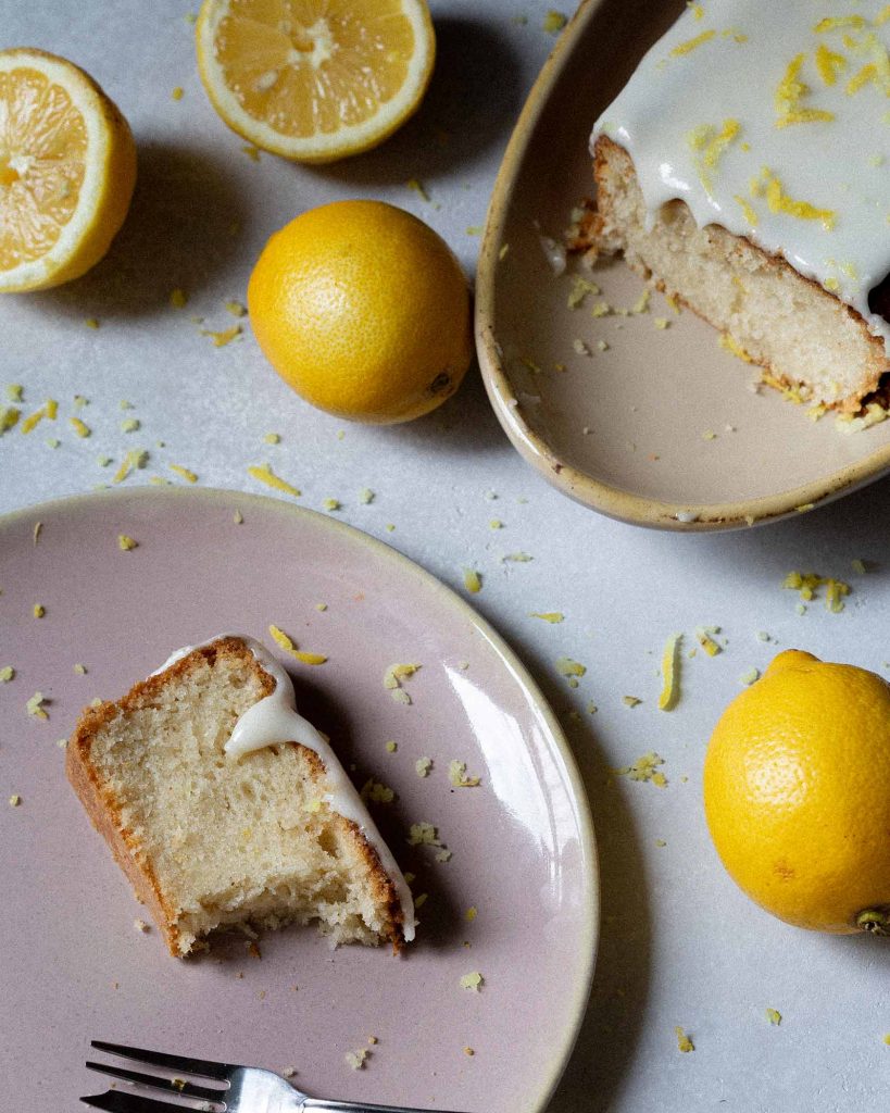 Veganer Zitronenkuchen mit Zuckerguss und Zitronenscheiben auf heller Platte