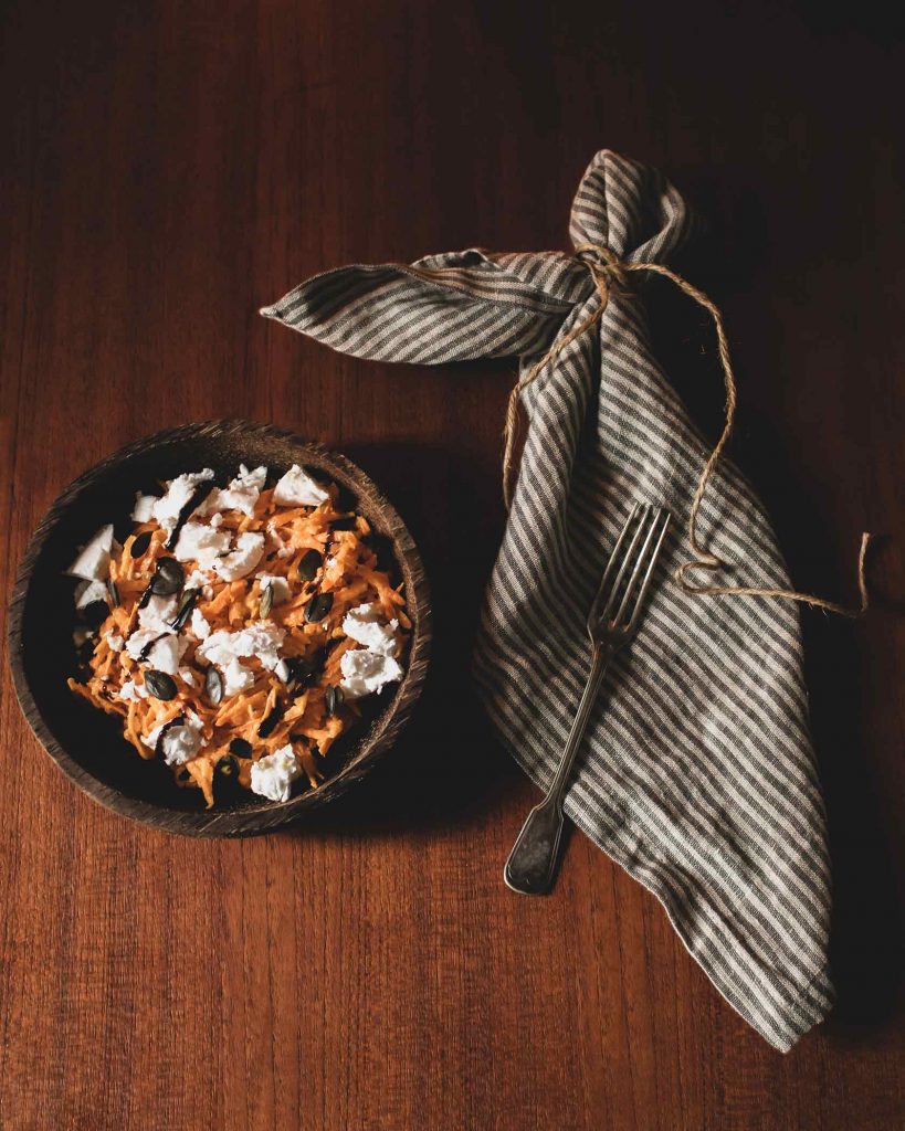 Frischer Karottensalat mit veganem Feta, Kürbiskernen und Balsamicocreme auf einem Teller angerichtet.