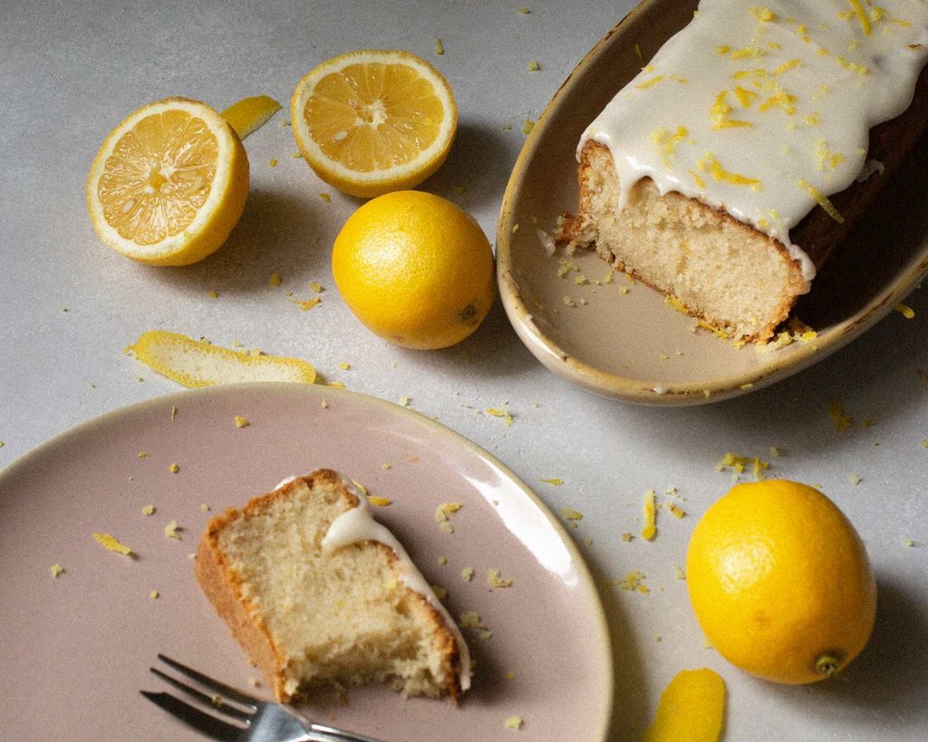 Veganer Zitronenkuchen mit Zuckerguss und Zitronenscheiben auf heller Platte