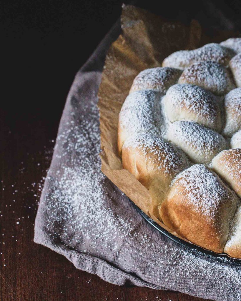 Goldbraune vegane Buchteln dicht aneinander gebacken und mit Puderzucker bestäubt