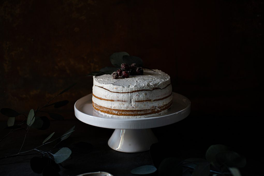 Vegane Torte mit Biskuitboden, weißer Schokoladencreme und Pflaumenmus, dekoriert auf einer Kuchenplatte