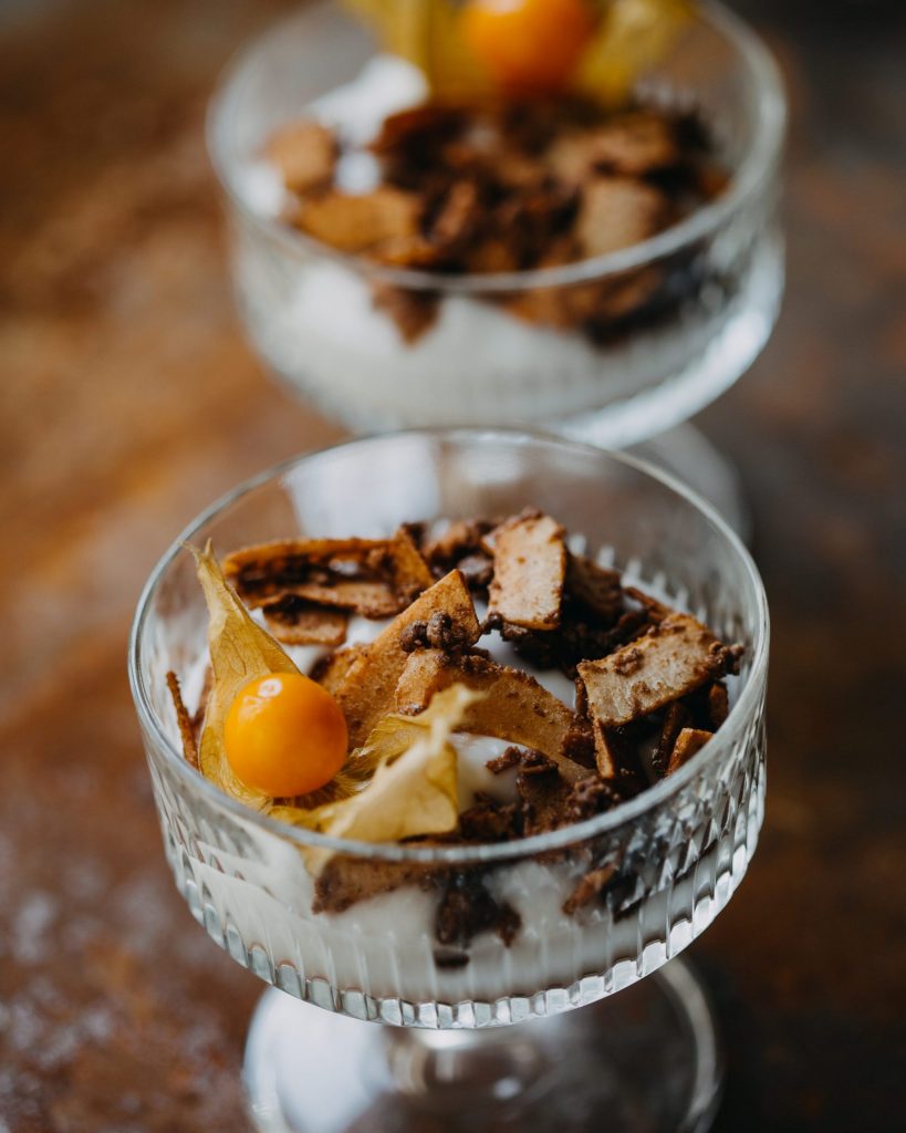 veganes Dessert aus Greek-Style-Joghurt mit karamellisierten Kokosflakes und Physalis im Glas serviert