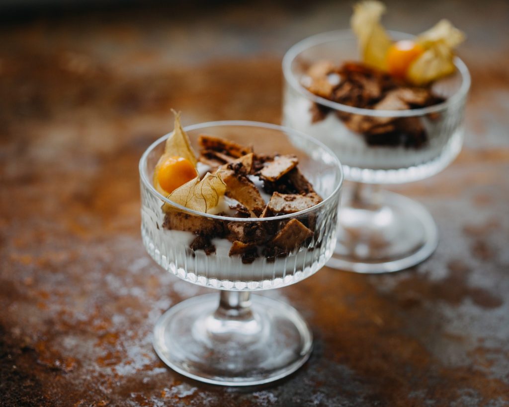 eganes Dessert aus Greek-Style-Joghurt mit karamellisierten Kokosflakes und Physalis im Glas serviert