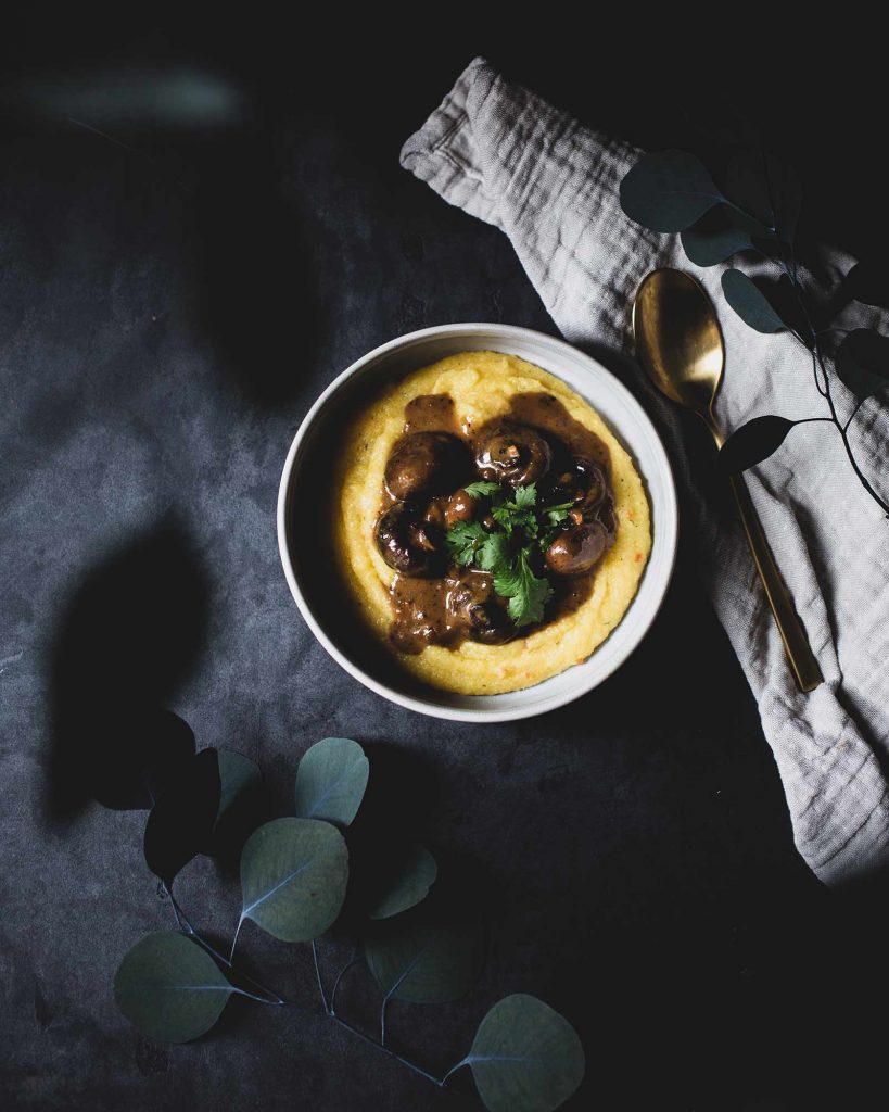 eganes Pilzgulasch Rezept mit cremiger Maispolenta auf einem Teller serviert.