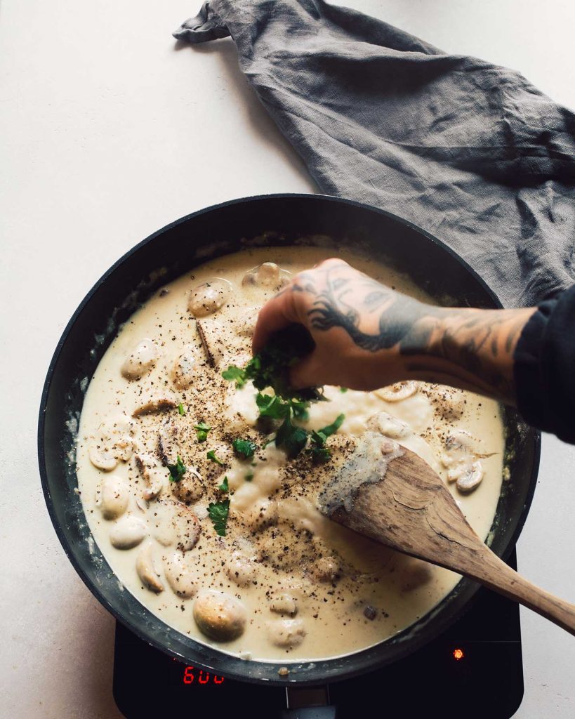 Vegane Spinatknödel serviert mit cremigen Rahmchampignons auf einem Teller