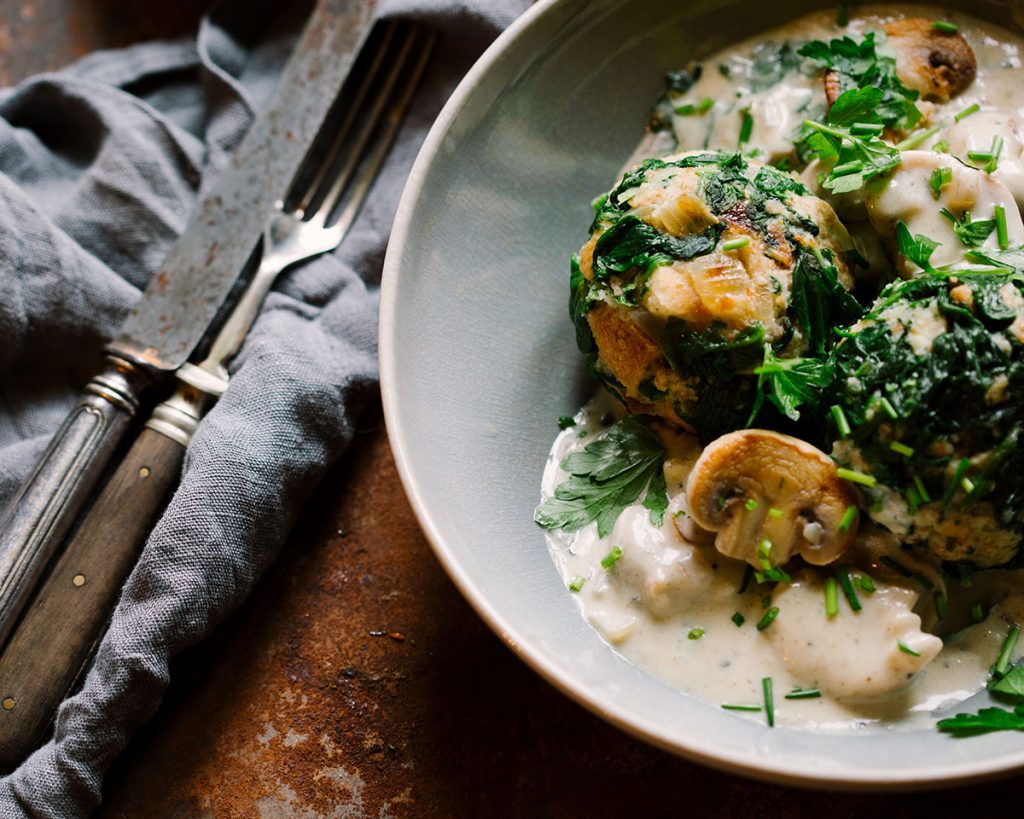 Vegane Spinatknödel serviert mit cremigen Rahmchampignons auf einem Teller