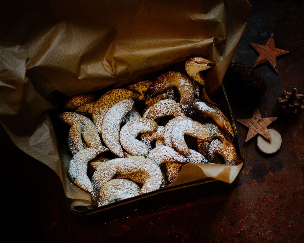 Vegane Vanillekipferl auf Backpapier mit Puderzucker bestäubt