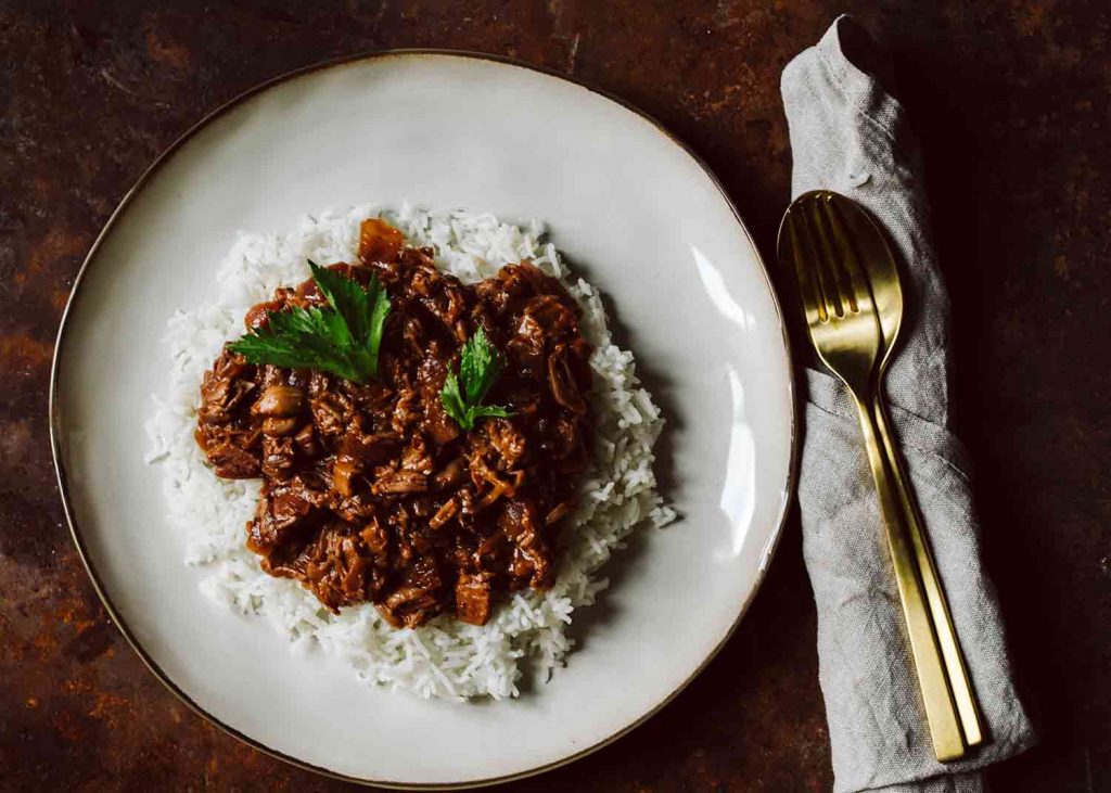 Veganes Jackfruitgulasch in dunkler Sauce serviert mit Beilage auf einem Teller